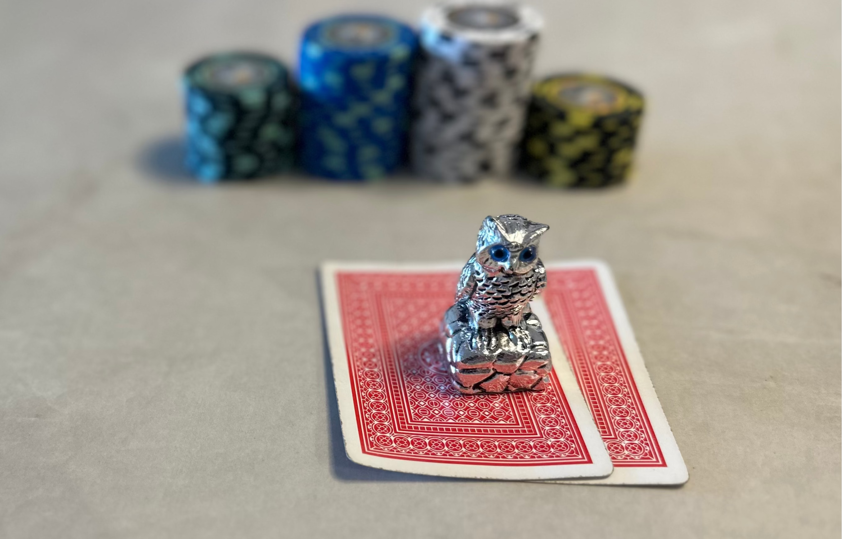 Small metal owl figurine on a red playing card with poker chips in the background.